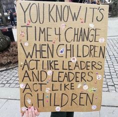 a woman holding up a sign that says you know it's time to change when children act like leaders and leaders act like children