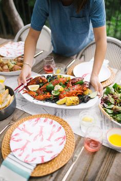 a woman sitting at a table covered in plates and bowls of food with lobsters on them