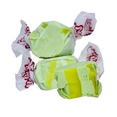 two pieces of green and yellow candy with white paper wrappers on top of them