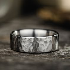 a wedding band made out of silver on top of a wooden table with rocks in the background