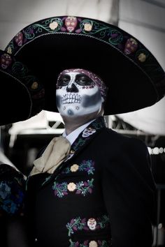 a man wearing a skeleton face paint and sombrero with flowers on his head