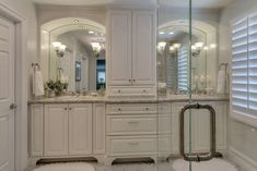 a large bathroom with white cabinets and marble counter tops, along with a glass enclosed shower stall