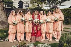 a group of women standing next to each other in front of some bushes and flowers