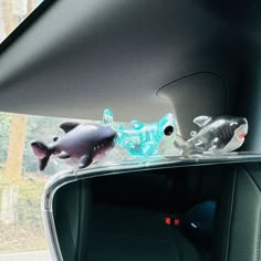 two plastic fish on the dashboard of a car, one is looking out the window