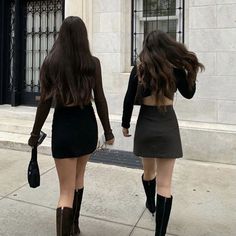 two women walking down the street in short skirts and knee high boots, both wearing black