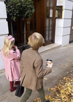 two children are walking down the sidewalk holding coffee cups