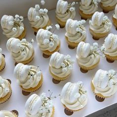 cupcakes with white frosting and flowers on them are arranged in a box