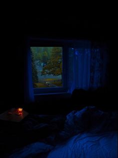 a dark room with a lit candle on the bed in front of an open window