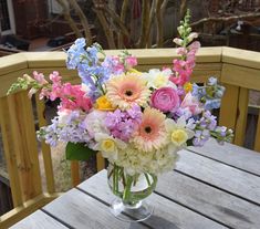 a vase filled with lots of colorful flowers on top of a wooden table next to a tree