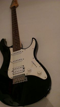 an electric guitar hanging on the wall in front of a white wall with black trim