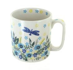 a blue and yellow dragonfly mug sitting on top of a white tablecloth covered table