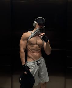 a shirtless man with headphones on taking a selfie in front of a mirror