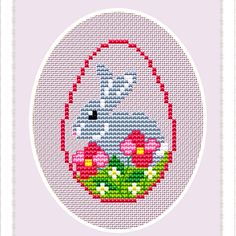 a cross stitch bunny in a basket with flowers on the bottom and an oval frame