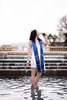 a woman wearing a blue sash drinking from a bottle in the middle of a fountain