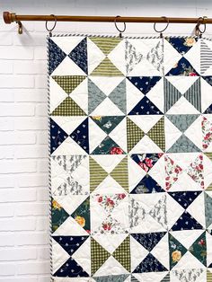 a quilt hanging on a brick wall next to a white brick wall with an iron rod