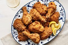 fried chicken on a blue and white plate with lemon wedges next to a glass of wine