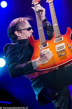 a man holding two electric guitars on stage