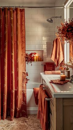 a bathroom with orange towels and candles on the counter next to the bathtub,