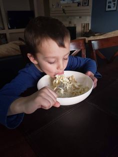 a young boy eating food out of a white bowl