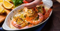 a person is dipping some shrimp into a casserole with lemons on the side