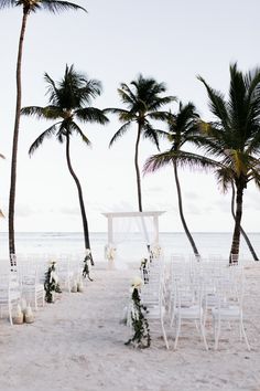 an outdoor wedding setup on the beach with white chairs and palm trees in the background