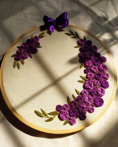 an embroidery project with purple flowers in the shape of a circle on a white surface