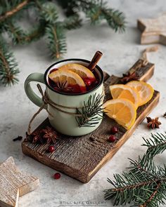 a cup of mulled with orange slices and cinnamon on a wooden tray surrounded by pine branches