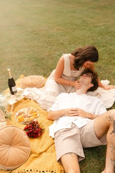 a man and woman laying on a blanket in the grass next to each other with food