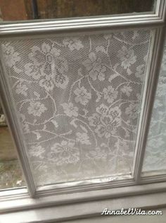 the window is covered with white lace and has flowers on it's glass panels