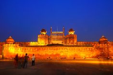 people are standing in front of a large building at night with bright lights on it