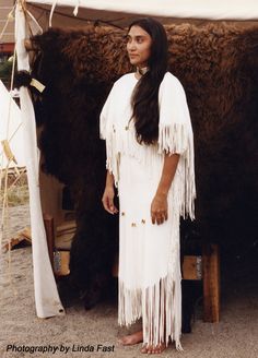 a native american woman standing in front of a black and white cow with long fringes