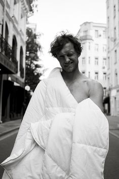 a man wrapped in a blanket walking down the street with his shirt over his shoulder