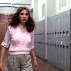 a woman walking down a hallway next to lockers in pink sweater and grey pants