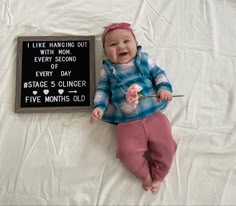 a baby laying on top of a bed next to a sign