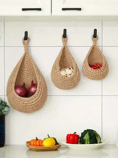 three baskets hanging on the wall with vegetables and fruit in them, along with other kitchen utensils