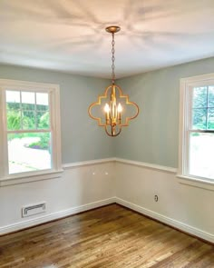 an empty room with two windows and a chandelier hanging from the ceiling,