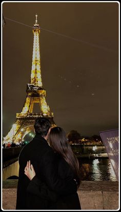 a man and woman are standing in front of the eiffel tower at night