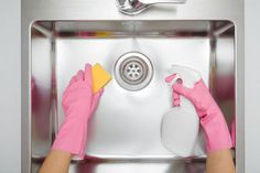 a person in pink gloves cleaning a stainless steel sink with a sponge and detergent