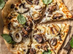 a pizza topped with mushrooms and spinach on top of a wooden cutting board next to a knife