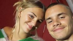 a man standing next to a woman in front of a red wall and smiling at the camera