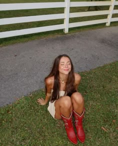 a woman sitting on the ground wearing red cowboy boots