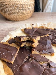 pieces of chocolate and peanut butter on top of a paper plate with a basket in the background