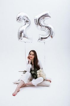 a woman sitting on the floor with balloons in front of her and number 25 balloon