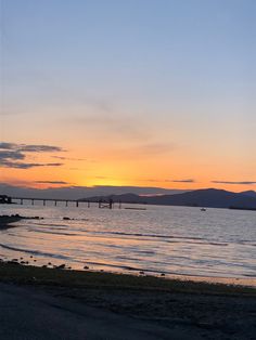 the sun is setting over the ocean with mountains in the background