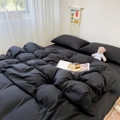 a teddy bear sitting on top of a bed with black comforter and pillows in front of a window