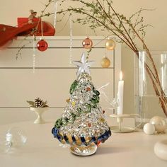 a glass christmas tree sitting on top of a table next to candles and other decorations