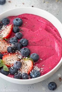 a bowl filled with blueberries and strawberries on top of a table next to other fruits