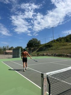 a shirtless man playing tennis on an outdoor court with blue sky and clouds in the background