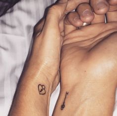 two people holding hands with tattoos on their wrists and wristbands in the shape of hearts