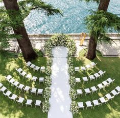 an outdoor ceremony setup with white chairs and greenery on the lawn by the water